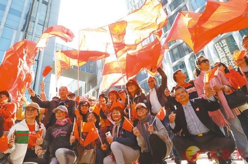 ■集會開始前參與人士面露笑容揮動手上的國旗，並在臉上貼上國旗的心形貼紙。 香港文匯報記者  攝
