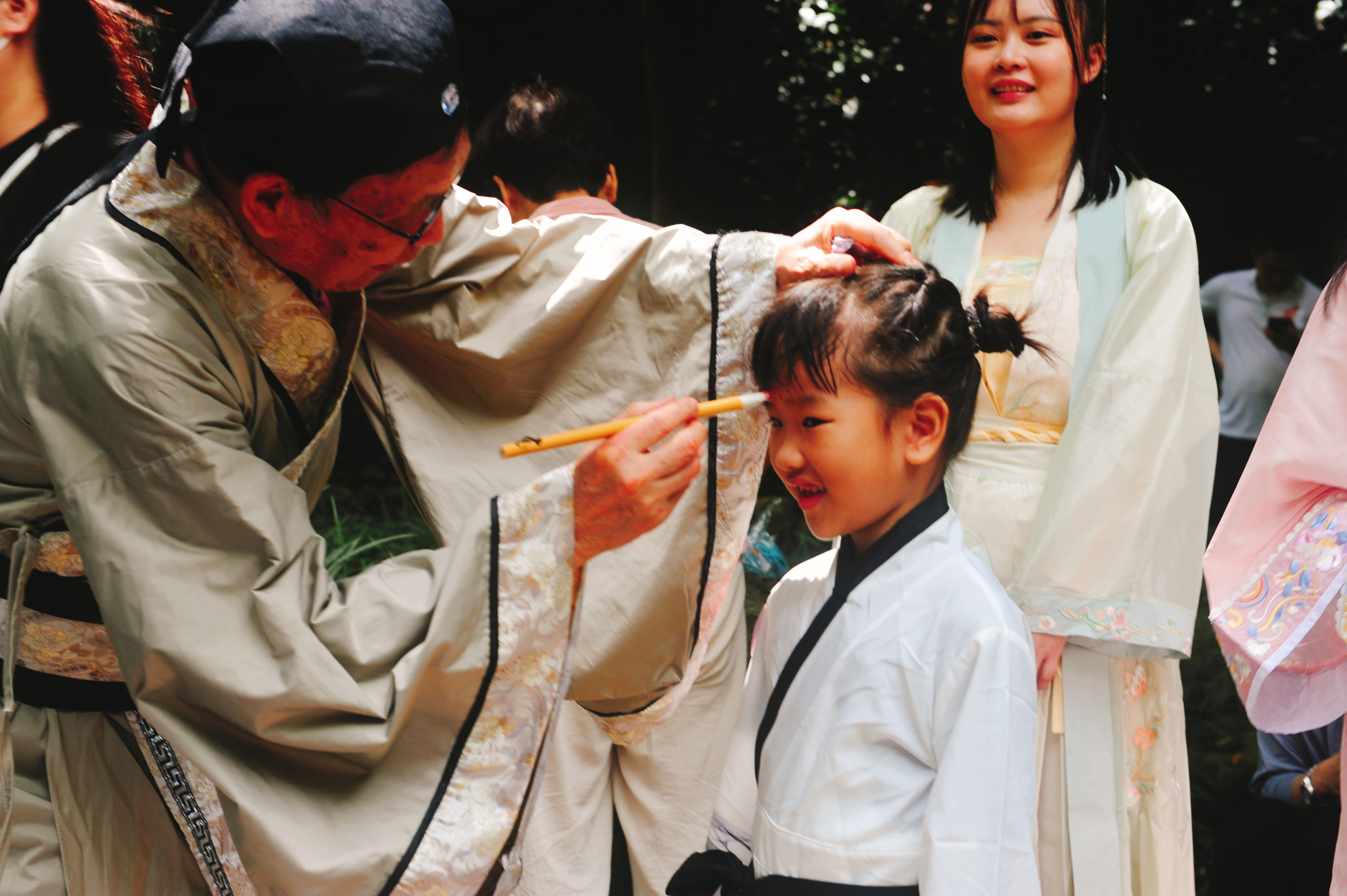 2、羅浮山文化研究會名譽會長謝澤南將蘸有朱砂的毛筆在每個學童的額頭正中央點上一顆紅痣，稱為點“聰明”.jpg